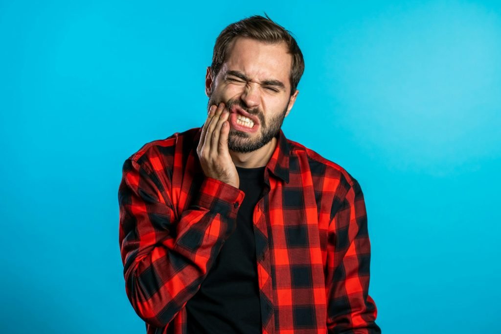 handsome man in red shirt with tooth pain on blue studio background. Toothache, dental